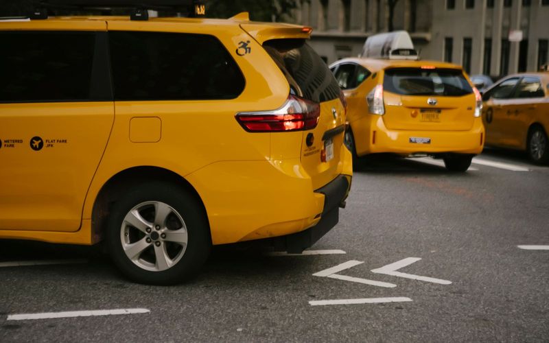 Modern yellow crossover taxi cars riding on asphalt road near commercial buildings in city